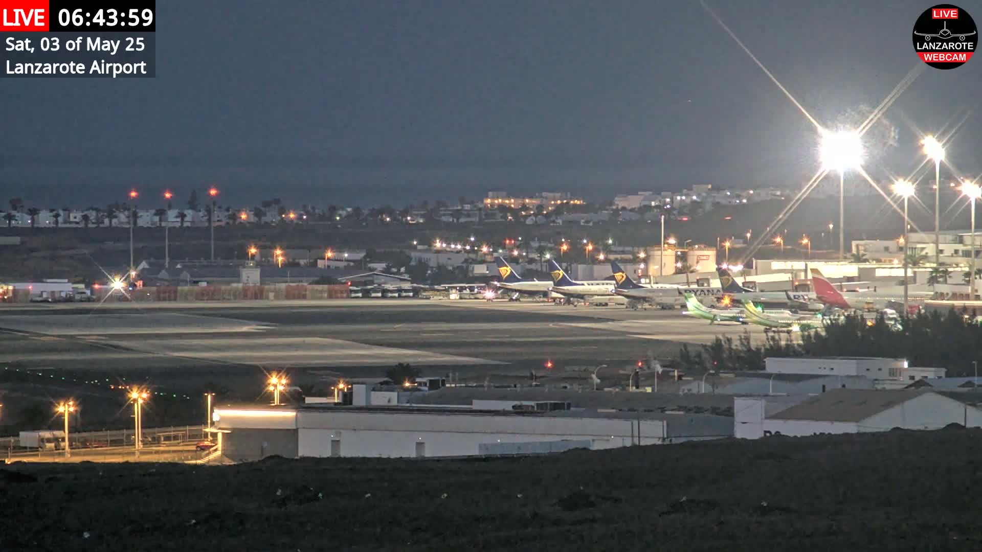 Several airplanes are parked on a dark airport tarmac at night under bright lights.