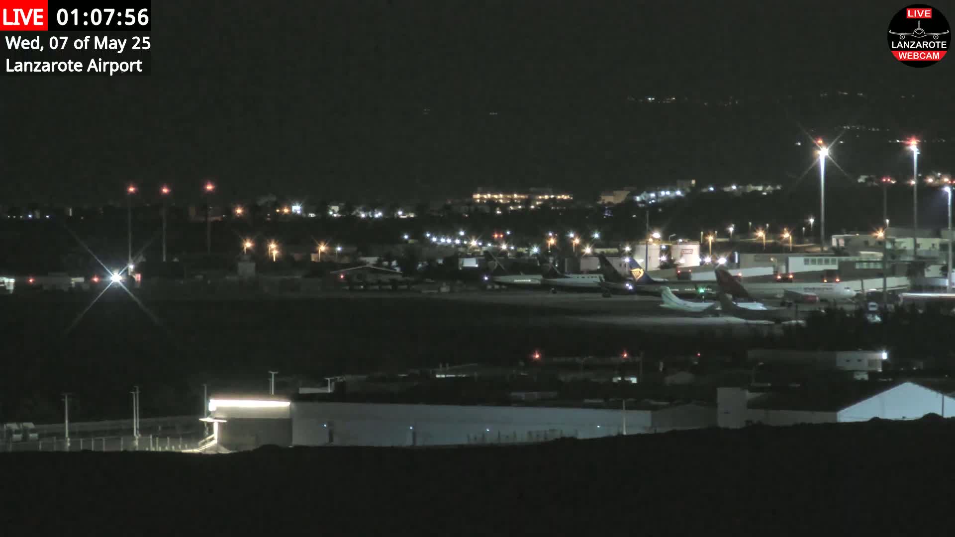 A nighttime view of an airport with several airplanes parked on the tarmac under a clear, dark sky.