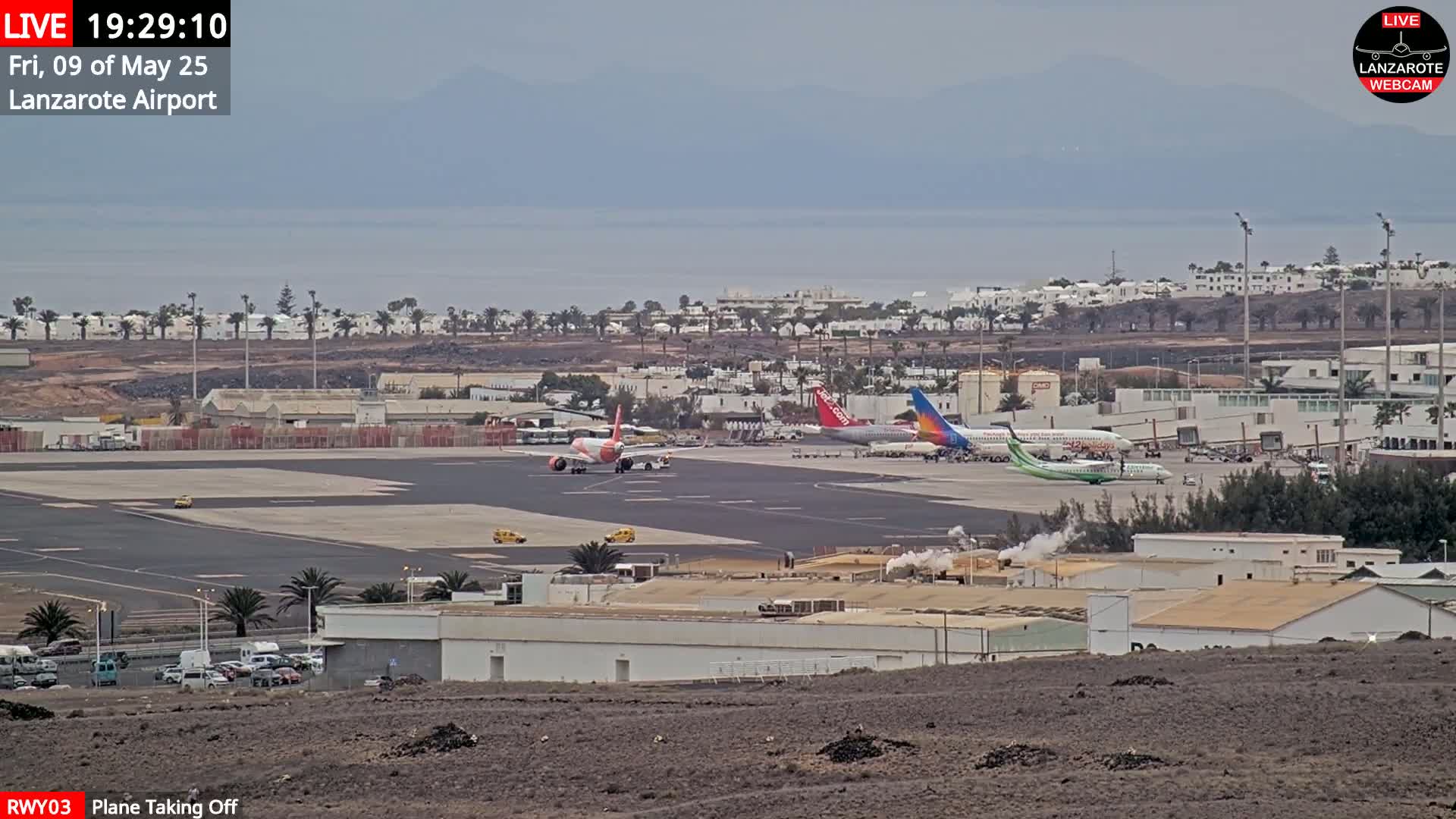 An airport tarmac with several airplanes, one of which is taking off, under an overcast sky.