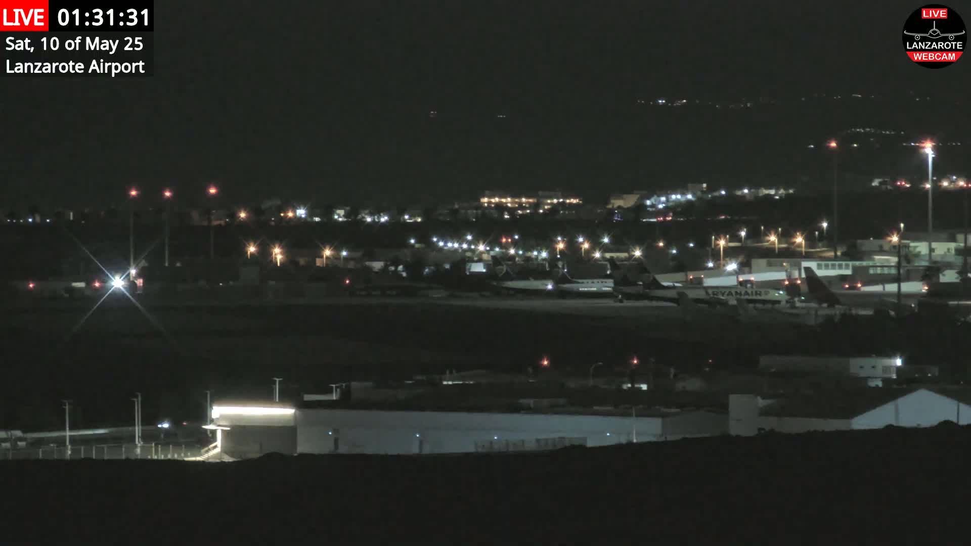 A nighttime long shot of an airport with several airplanes parked on the tarmac under a clear, dark sky.