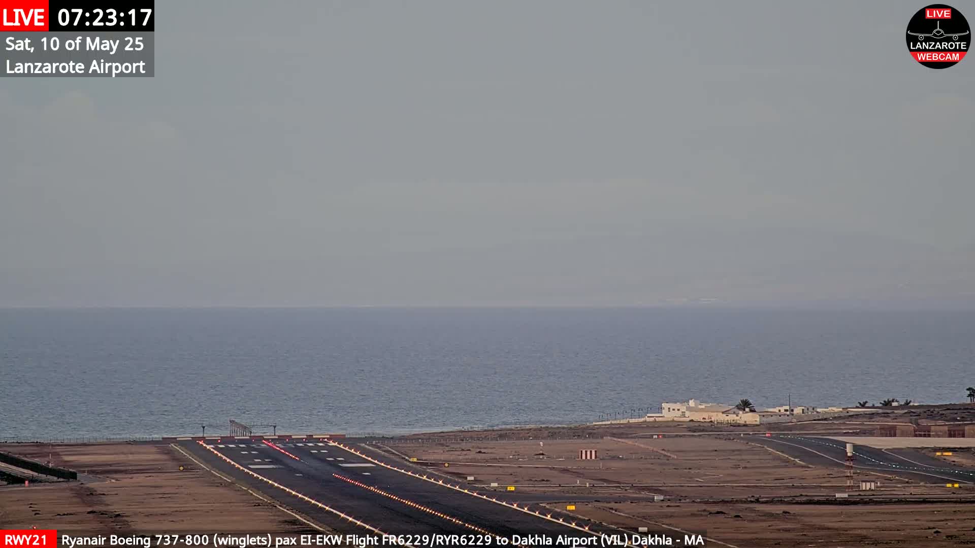 A hazy view of an airport runway next to a calm ocean under an overcast sky.
