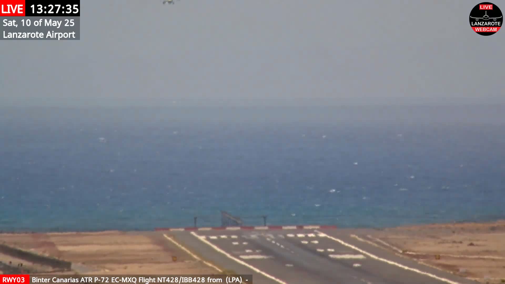 An airport runway extends toward a hazy, blue ocean under a mostly clear sky.