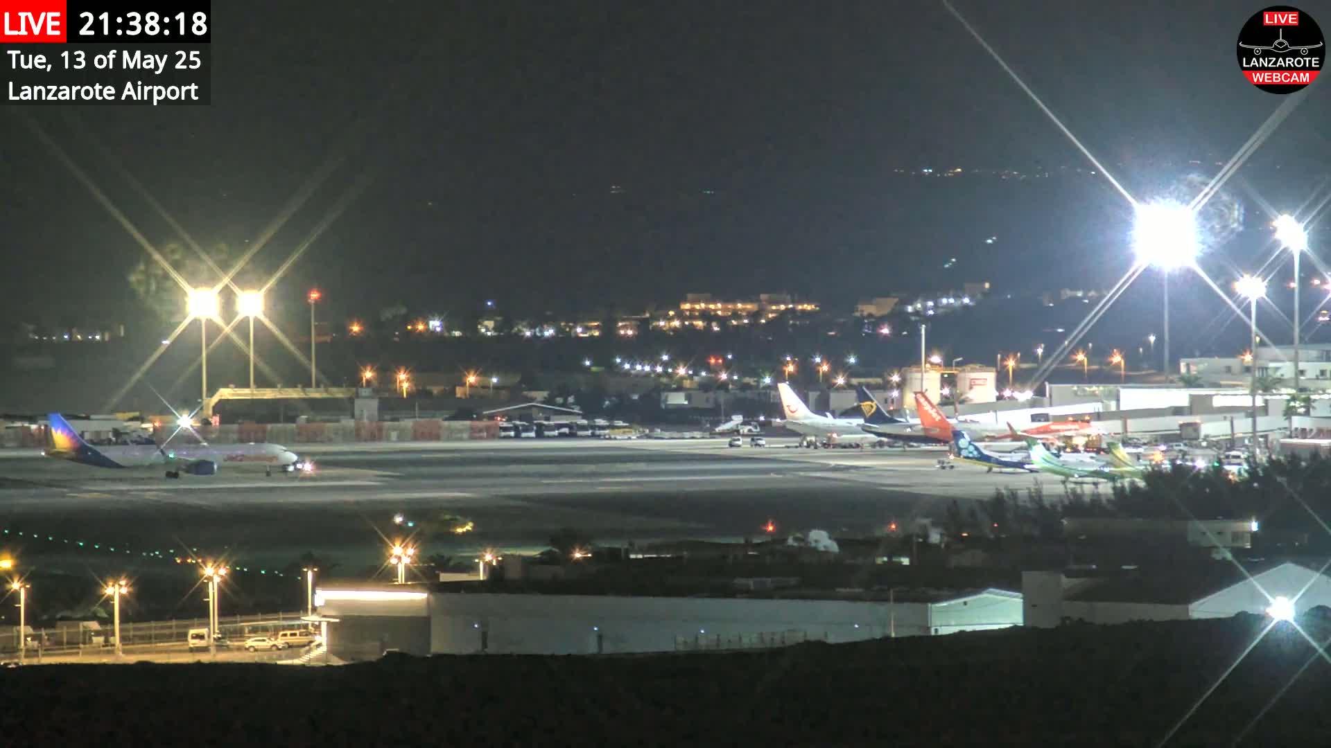 Several airplanes are parked on a brightly lit airport tarmac at night.