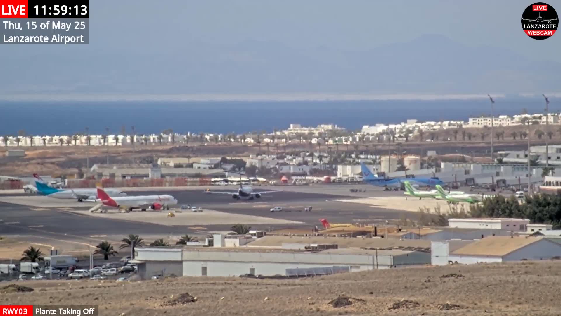Several airplanes are parked and taxiing on an airport tarmac near a calm ocean under a mostly clear sky.
