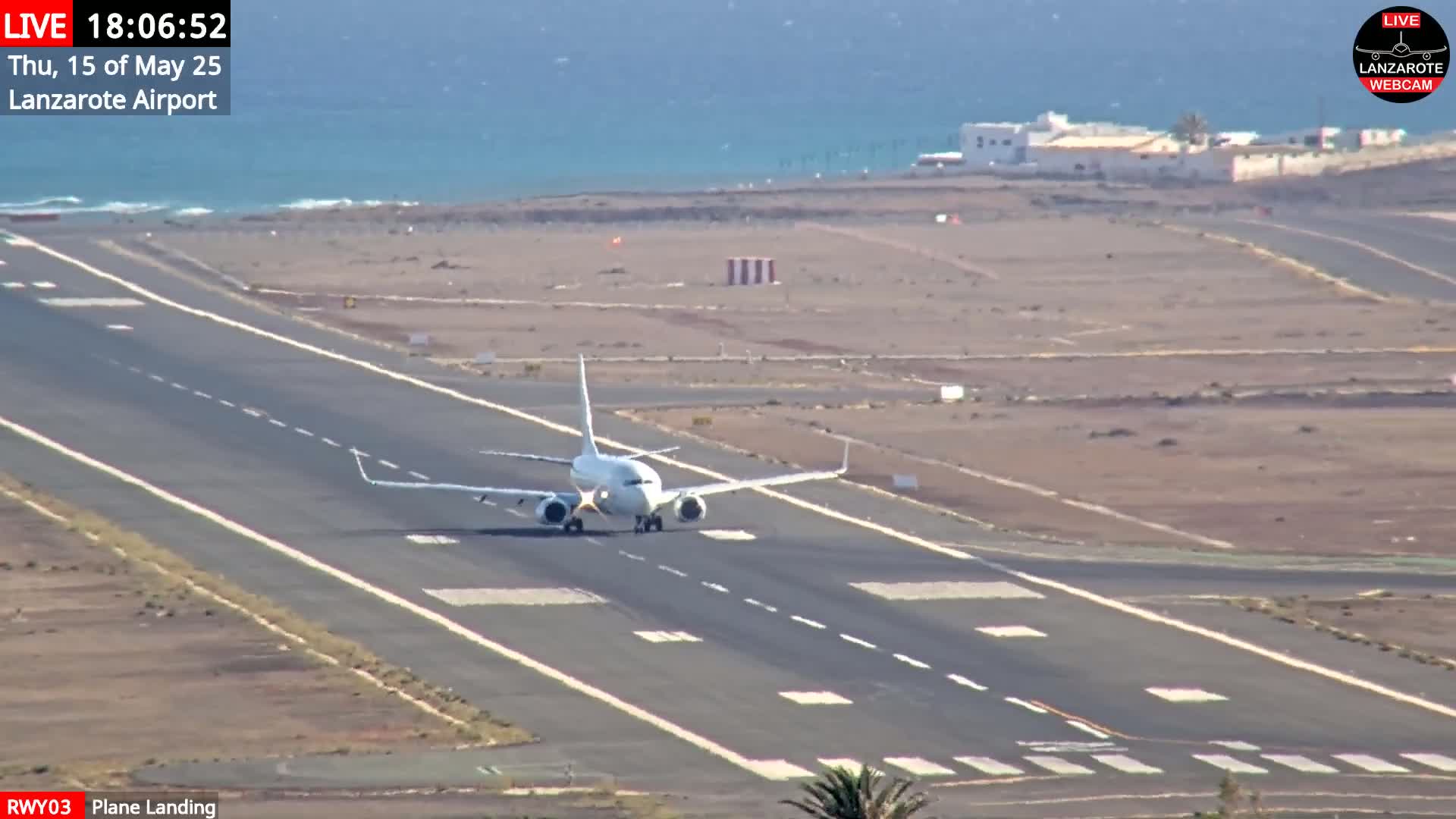A white airplane is landing on a runway near a body of water under sunny skies.