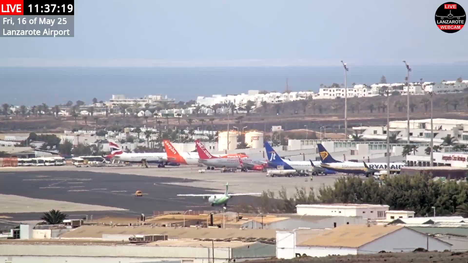 Several airplanes are parked on an airport tarmac near a body of water under sunny skies.