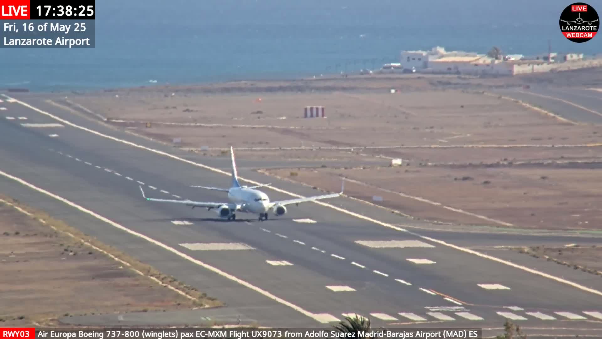 A passenger plane taxis on a runway near an ocean under a mostly clear sky.