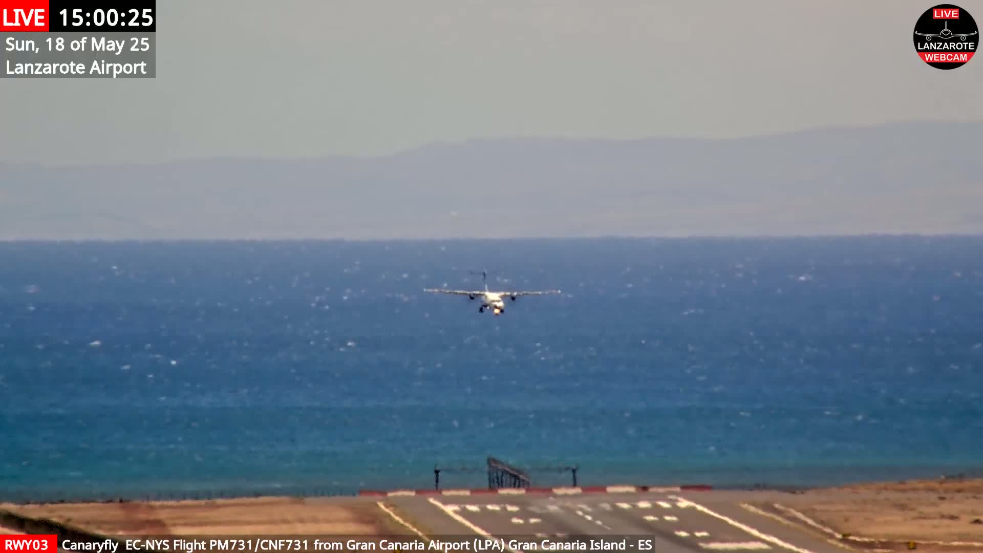 A small airplane is approaching a runway that borders a calm ocean under a hazy sky.