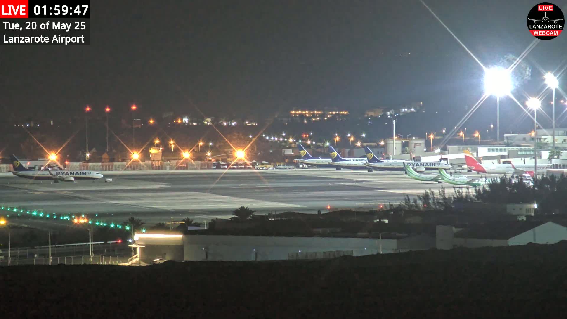 Several airplanes are parked on a brightly lit airport tarmac at night.