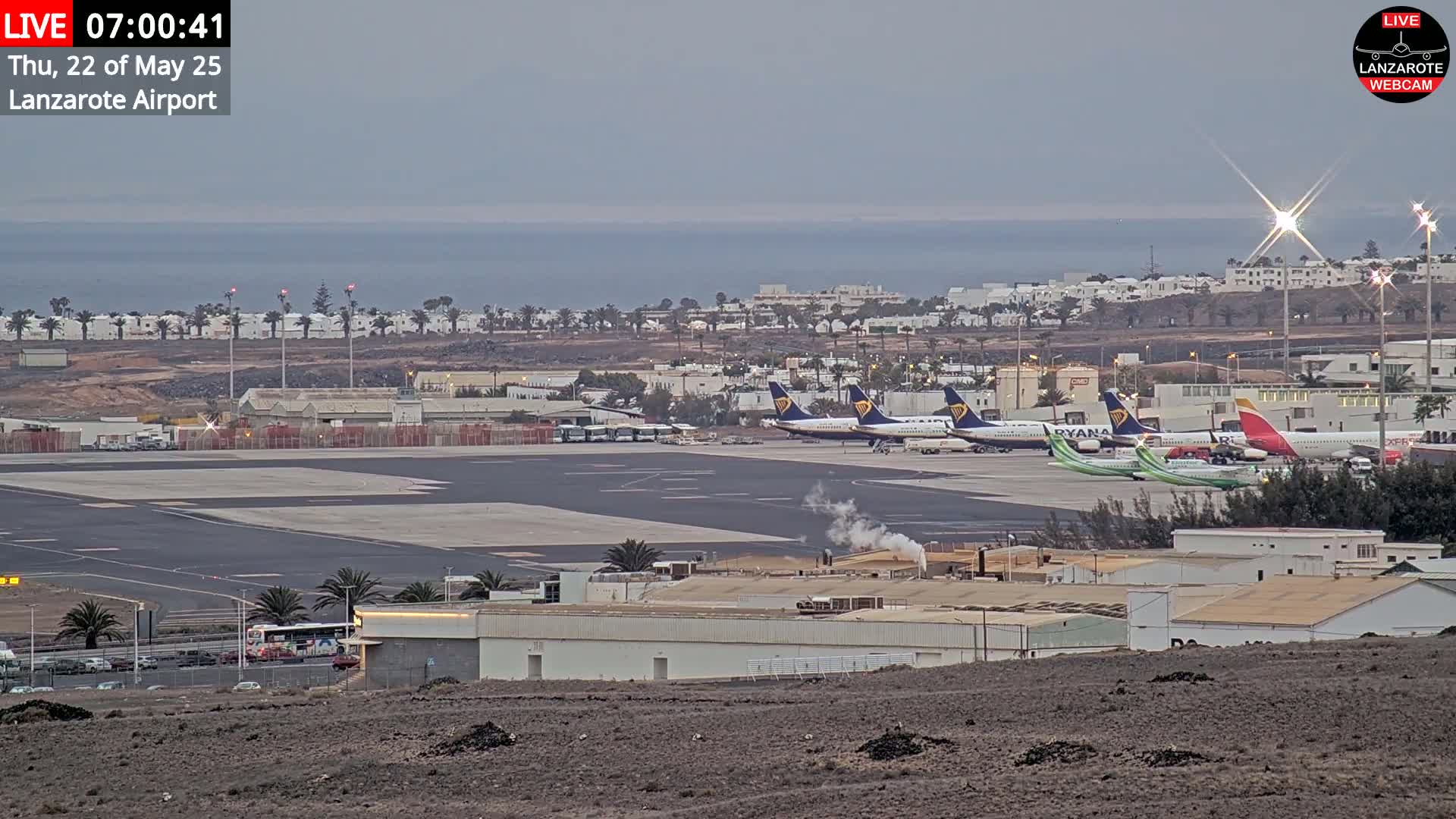 Several airplanes are parked on an airport tarmac near a calm ocean under an overcast sky.