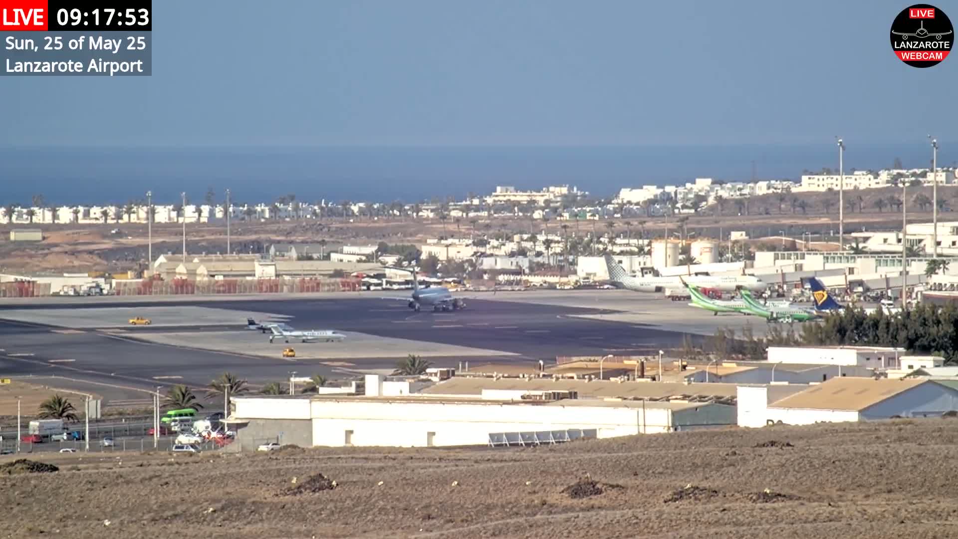 Several airplanes are on the tarmac of an airport near a body of water under a clear sky.