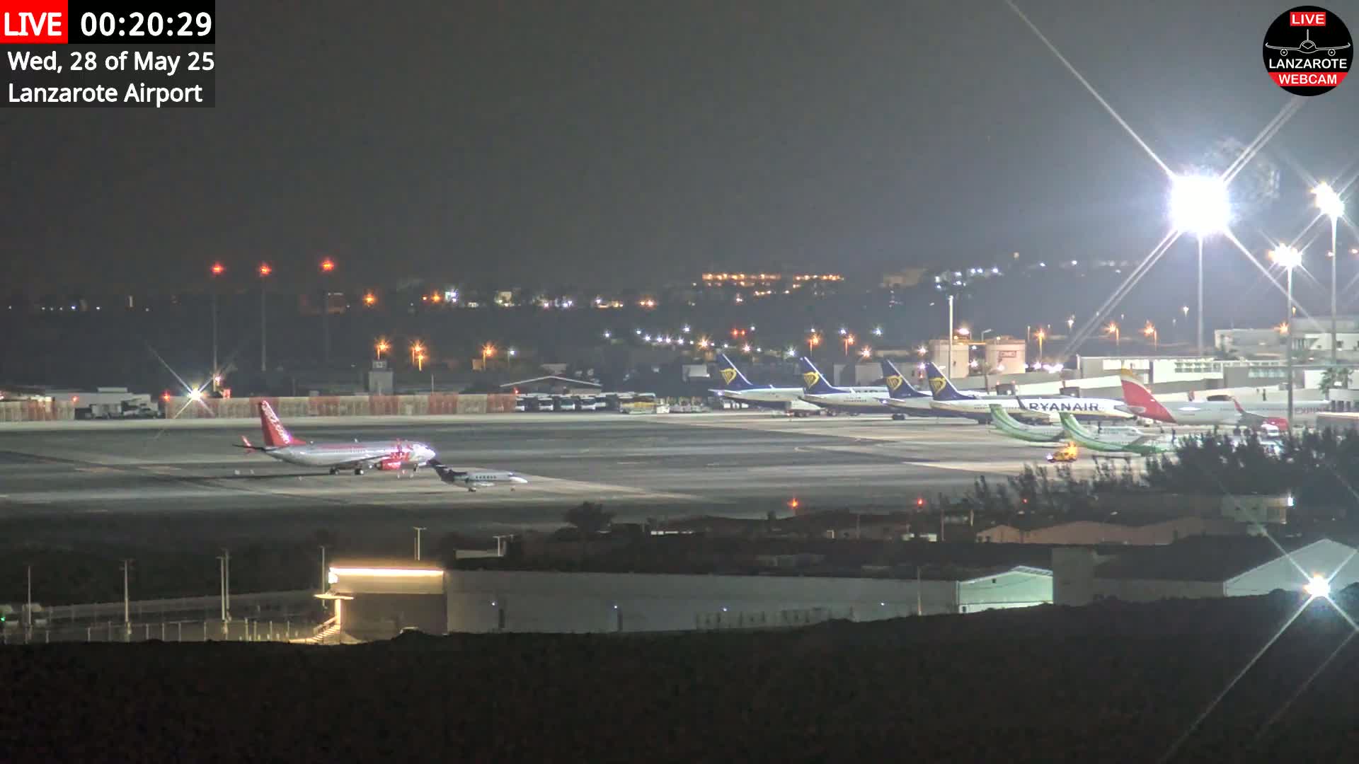 At night, several airplanes are parked on a brightly lit airport tarmac.