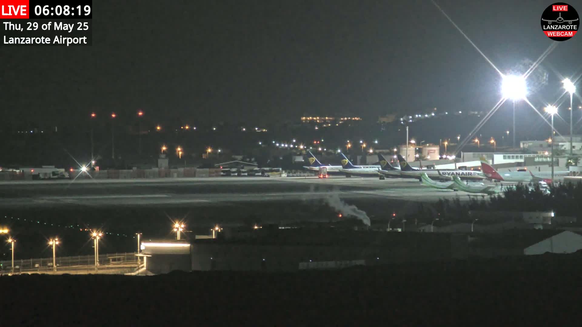 A nighttime view of several airplanes parked on an airport tarmac under bright lights.