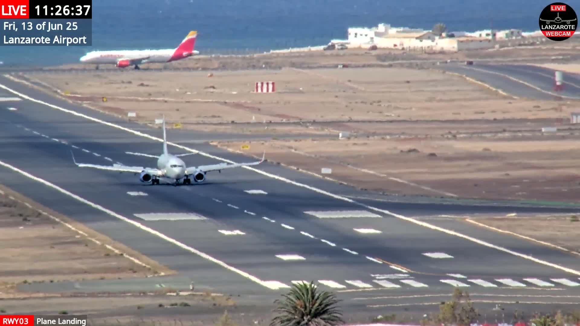 A plane is landing on a runway at an airport near a body of water under sunny conditions.
