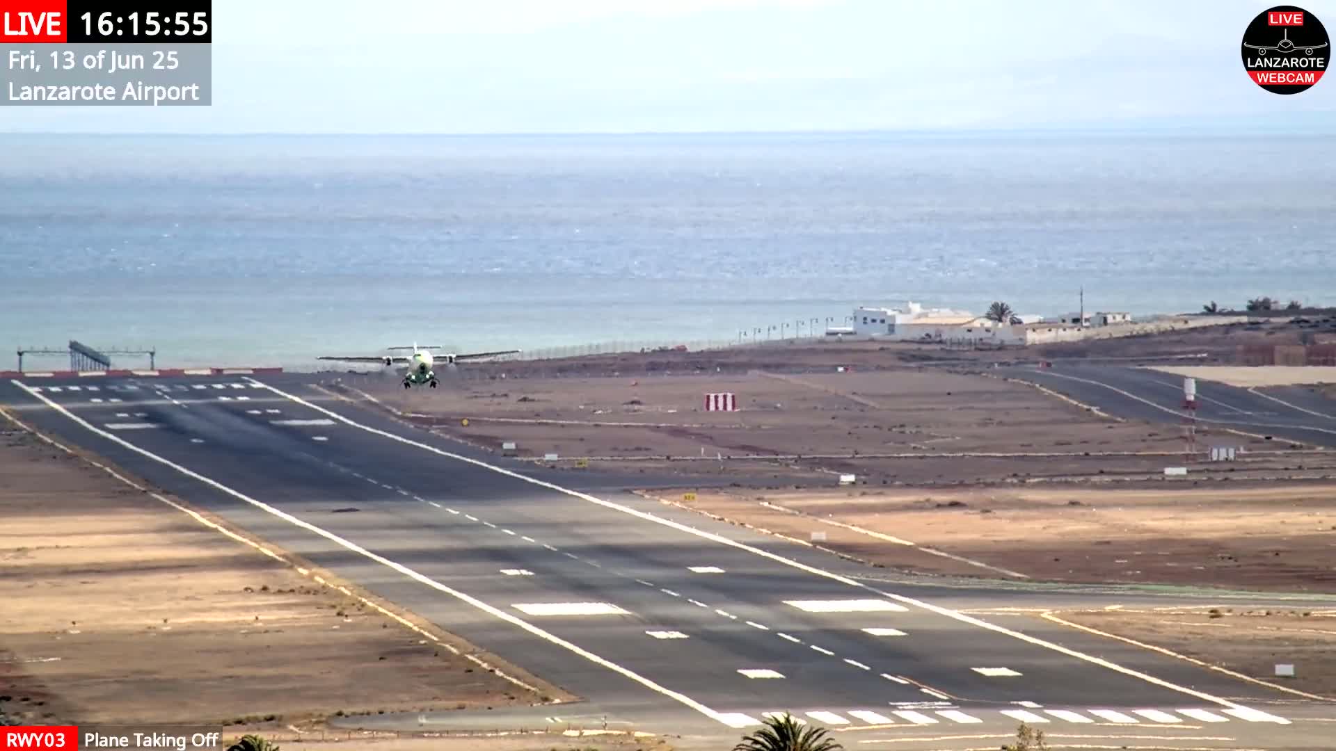 A small plane is taking off from a runway next to a body of water under a mostly clear sky.