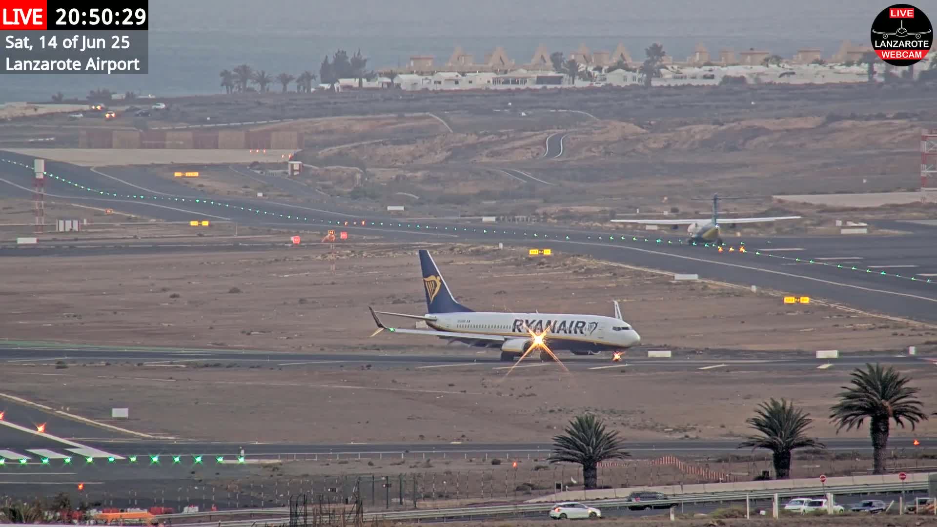 A sunny, hazy day at an airport shows several airplanes on the tarmac, with the ocean visible in the background.