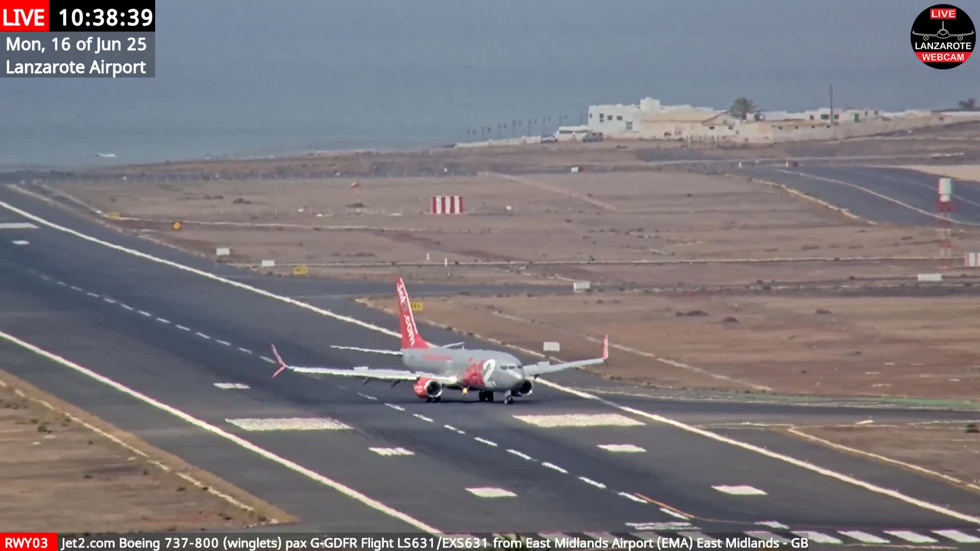 A jet plane taxis on a runway at an airport next to a calm ocean under a hazy sky.