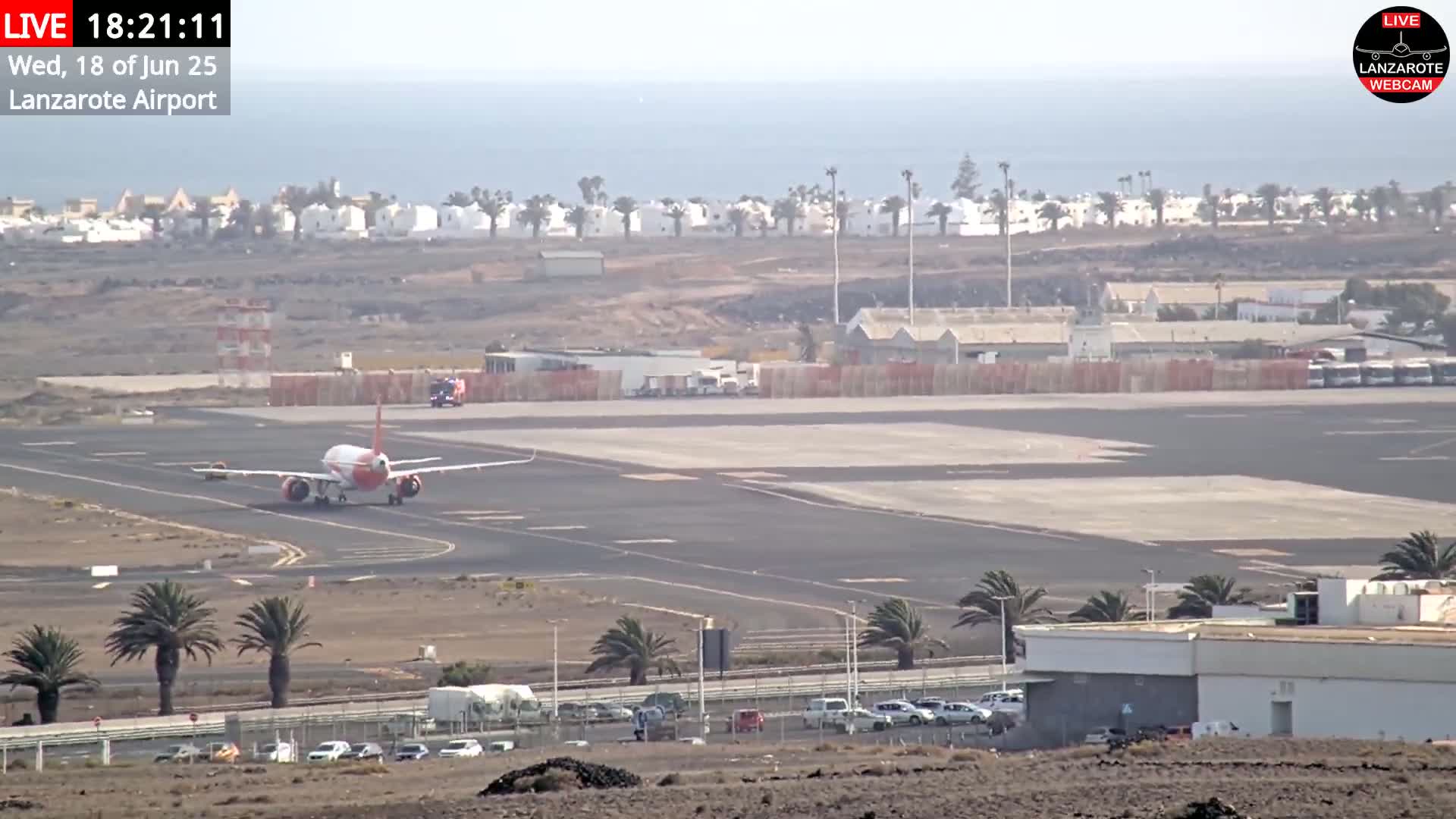 A red and white airplane taxis on an airport runway near a coastline under a hazy sky.