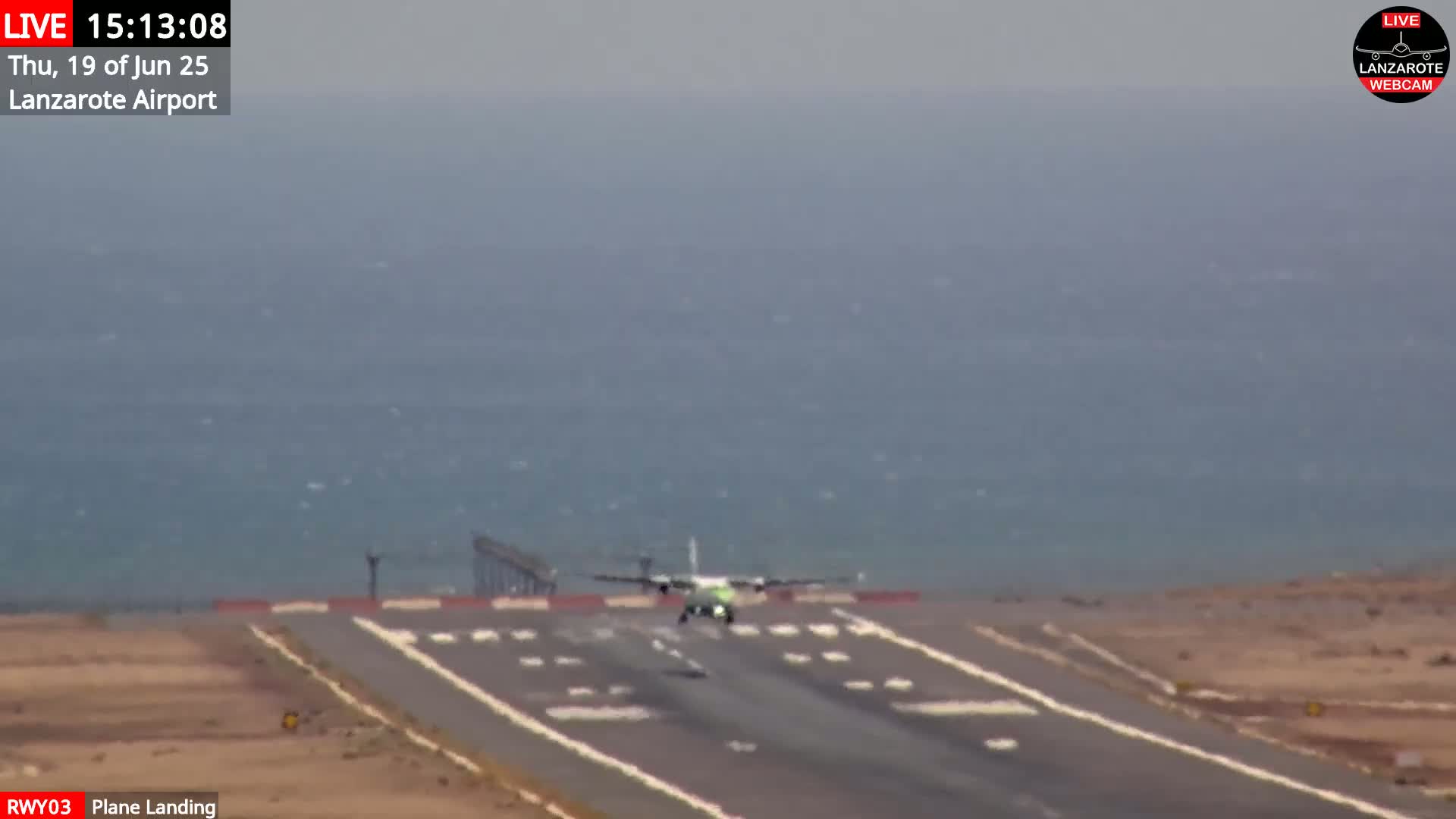 A plane is landing on a runway next to a body of water on a hazy day.