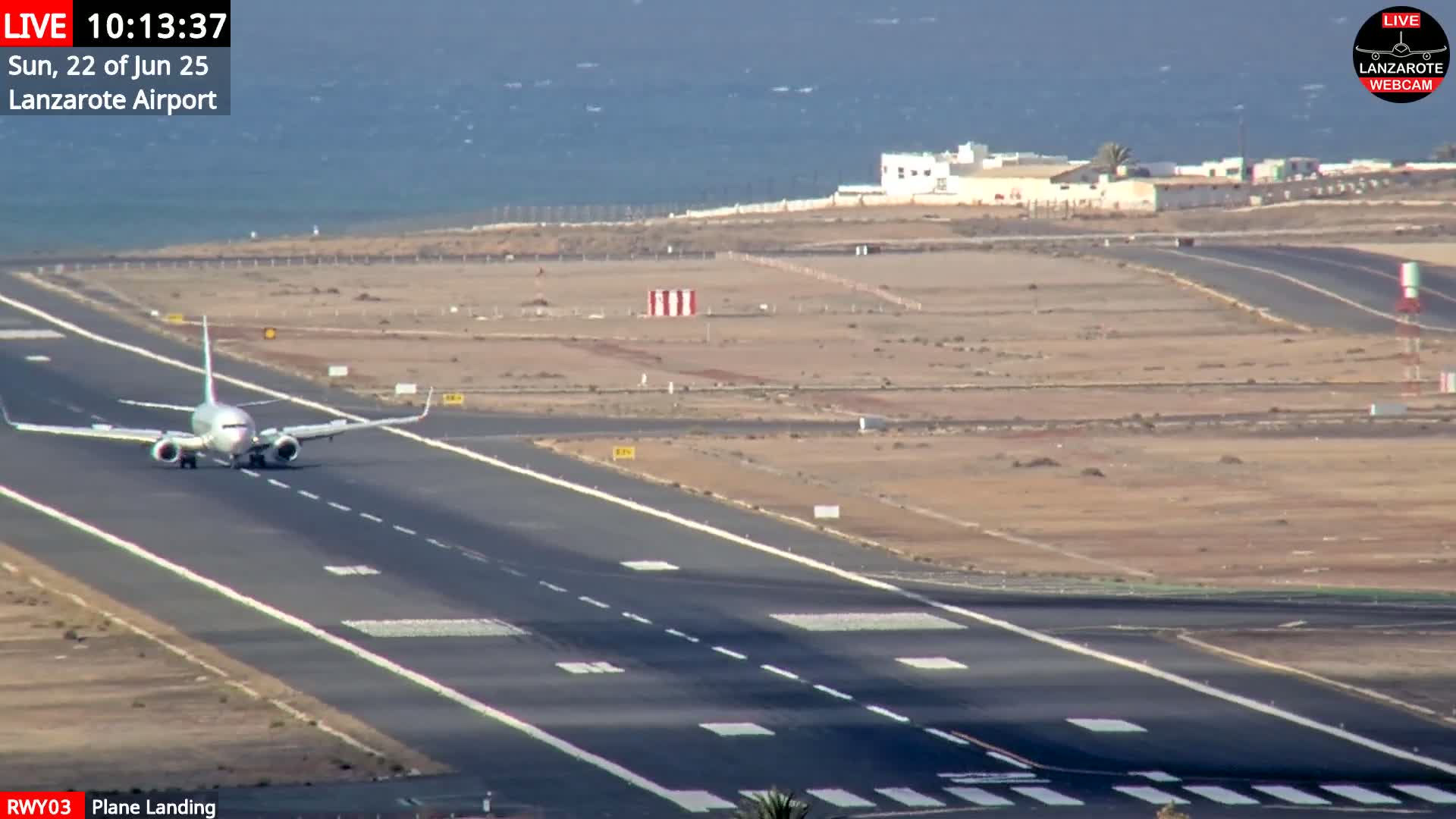 A commercial airplane is landing on a runway near a body of water under sunny conditions.