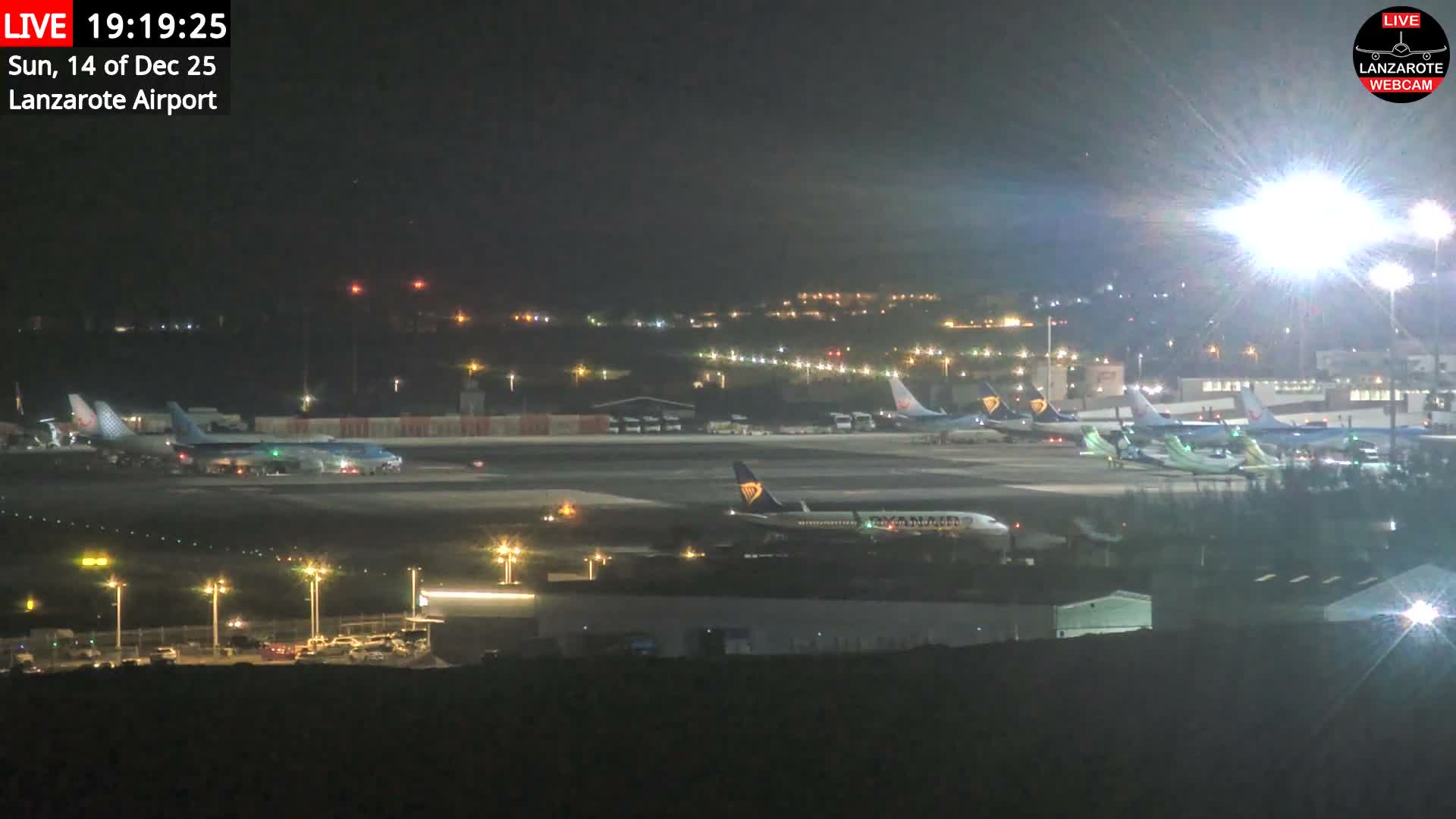 A commercial airplane with bright, starburst landing lights is centered on an airport runway next to the ocean under a gloomy, overcast sky.
