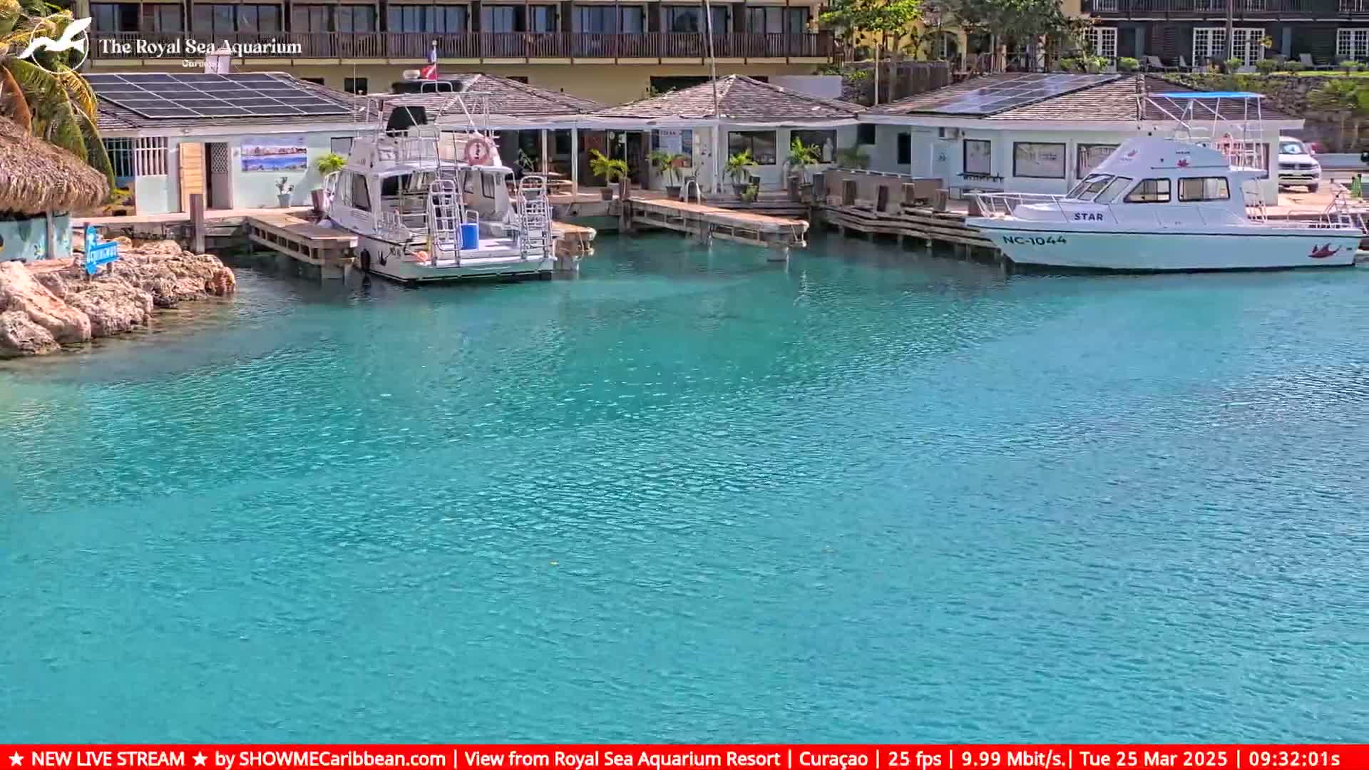 Two boats are docked at a marina next to a building, in calm, clear, turquoise water.
