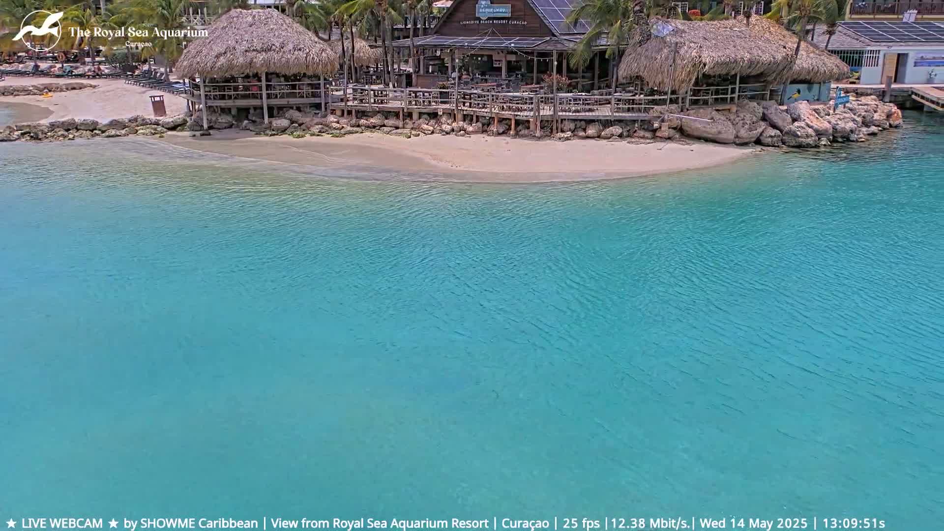 A beach with turquoise water and two thatched-roof structures is visible, with calm weather conditions.