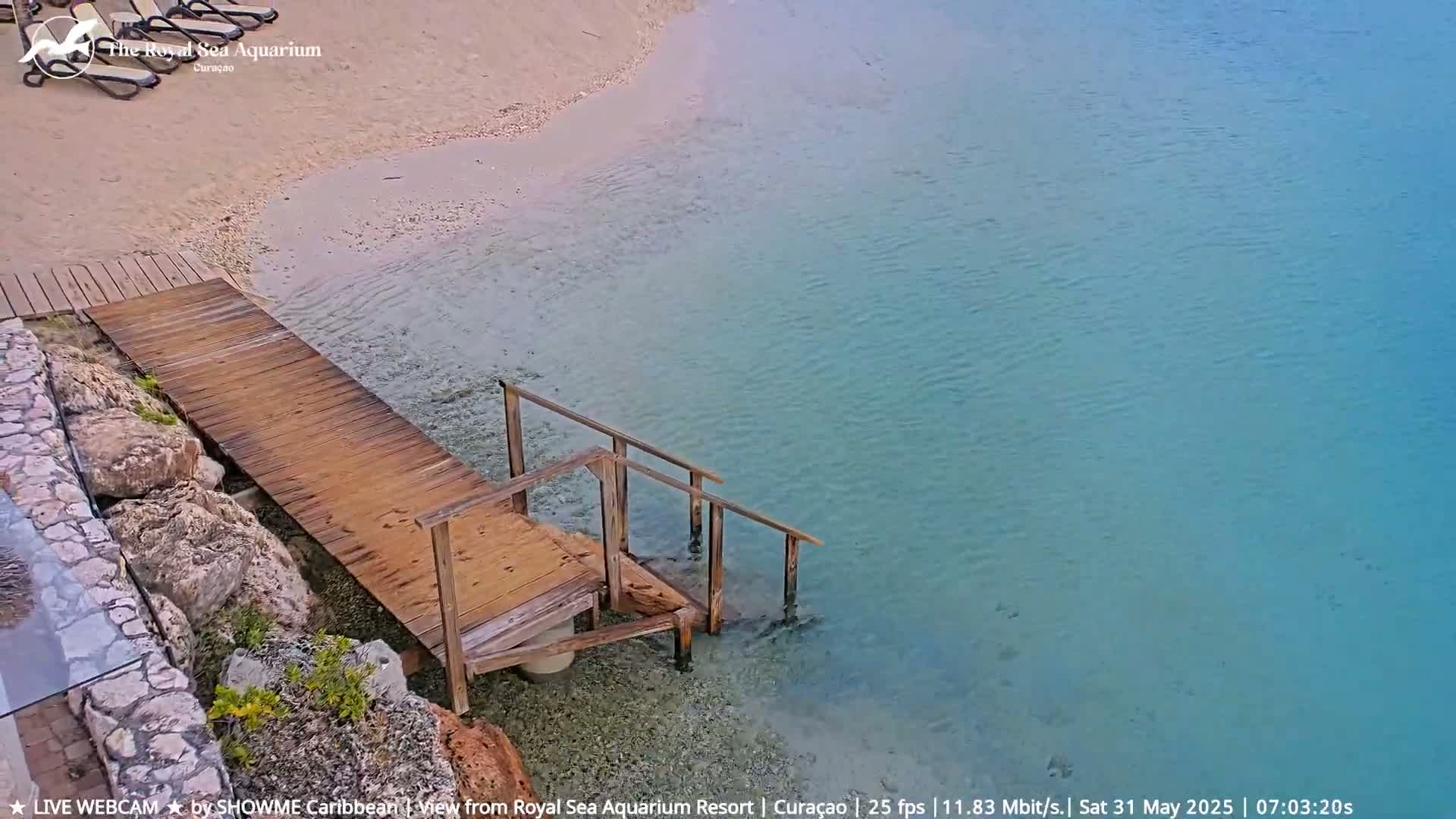 A wooden walkway with stairs leads from a sandy beach into calm, clear turquoise water.