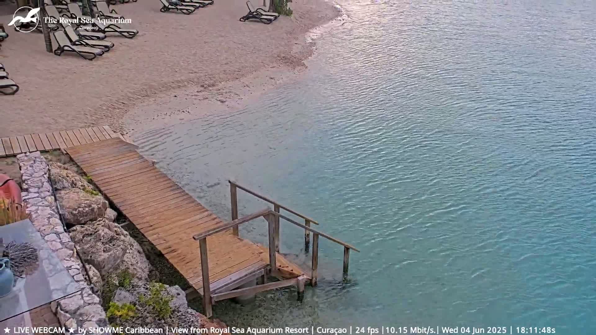 A wooden boardwalk and steps lead from a sandy beach into calm, teal-colored water.