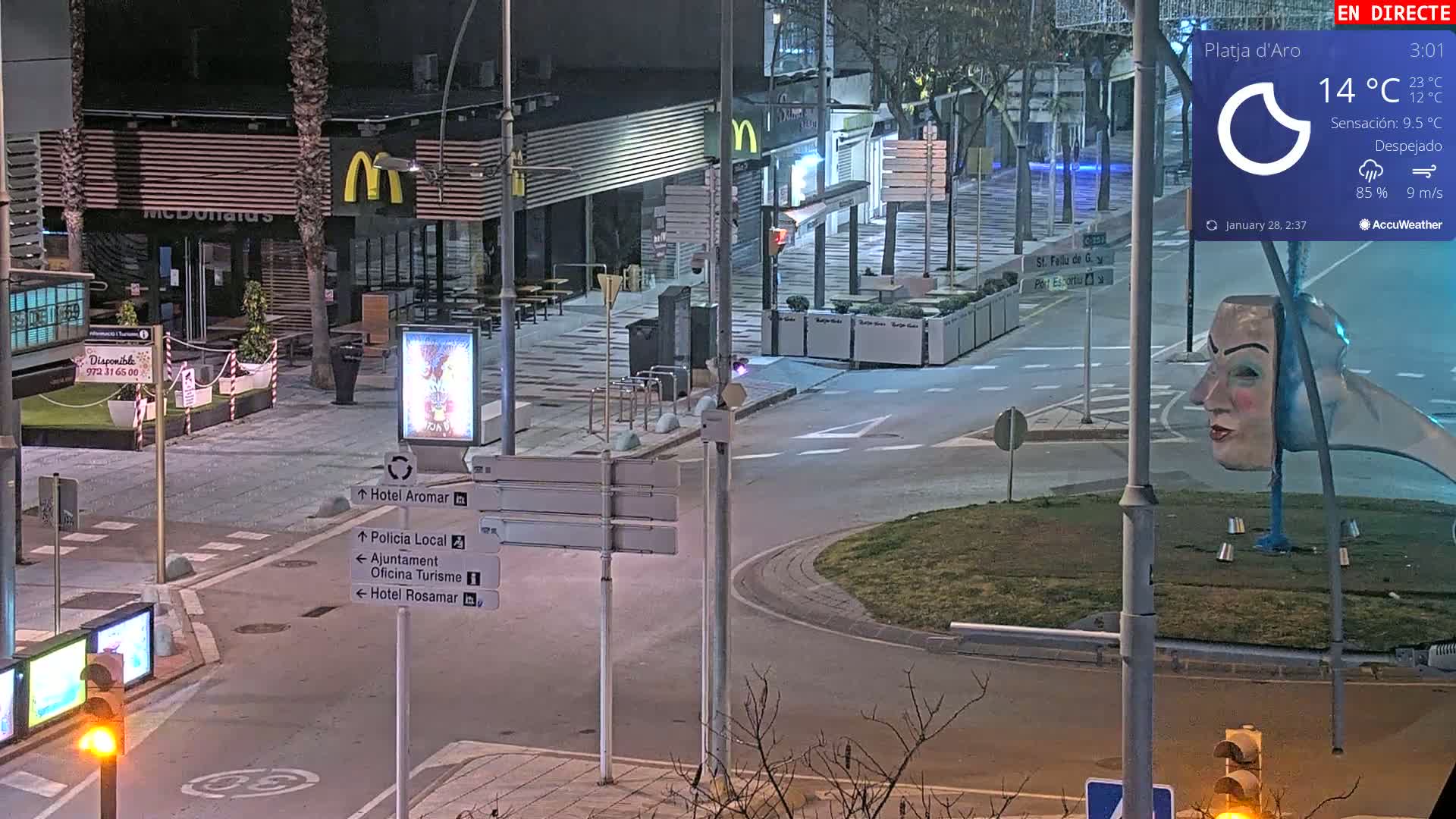 A nighttime street scene shows a McDonald's, signage pointing to various locations, a roundabout, and a sculpture of a woman's face, under clear, cool skies with a 14°C temperature.
