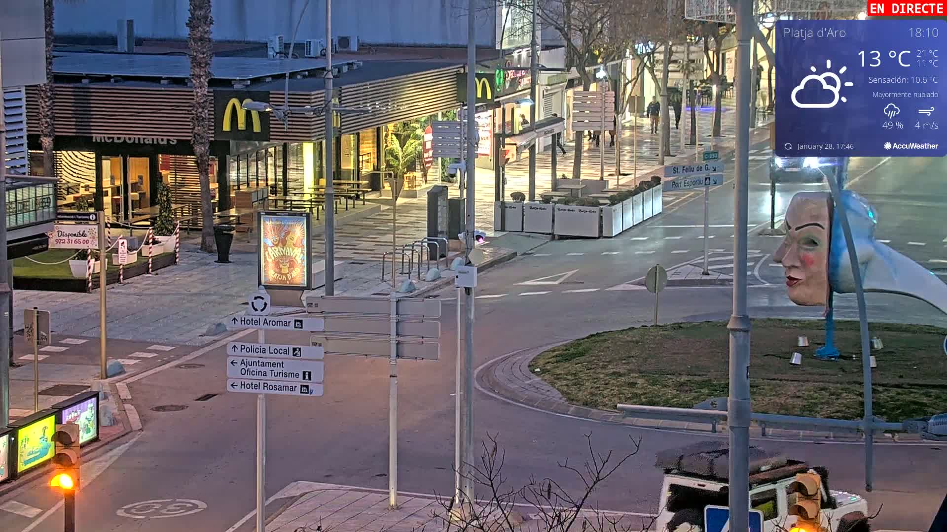 A mostly cloudy evening scene shows a street intersection with a McDonald's restaurant, street signs, and a large sculpture of a woman's head.