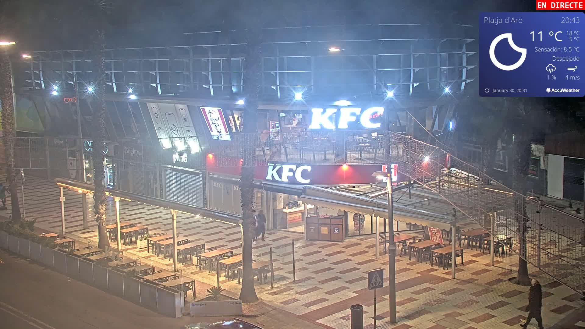 A mostly empty outdoor seating area at night in front of a KFC, under a clear, cool sky.