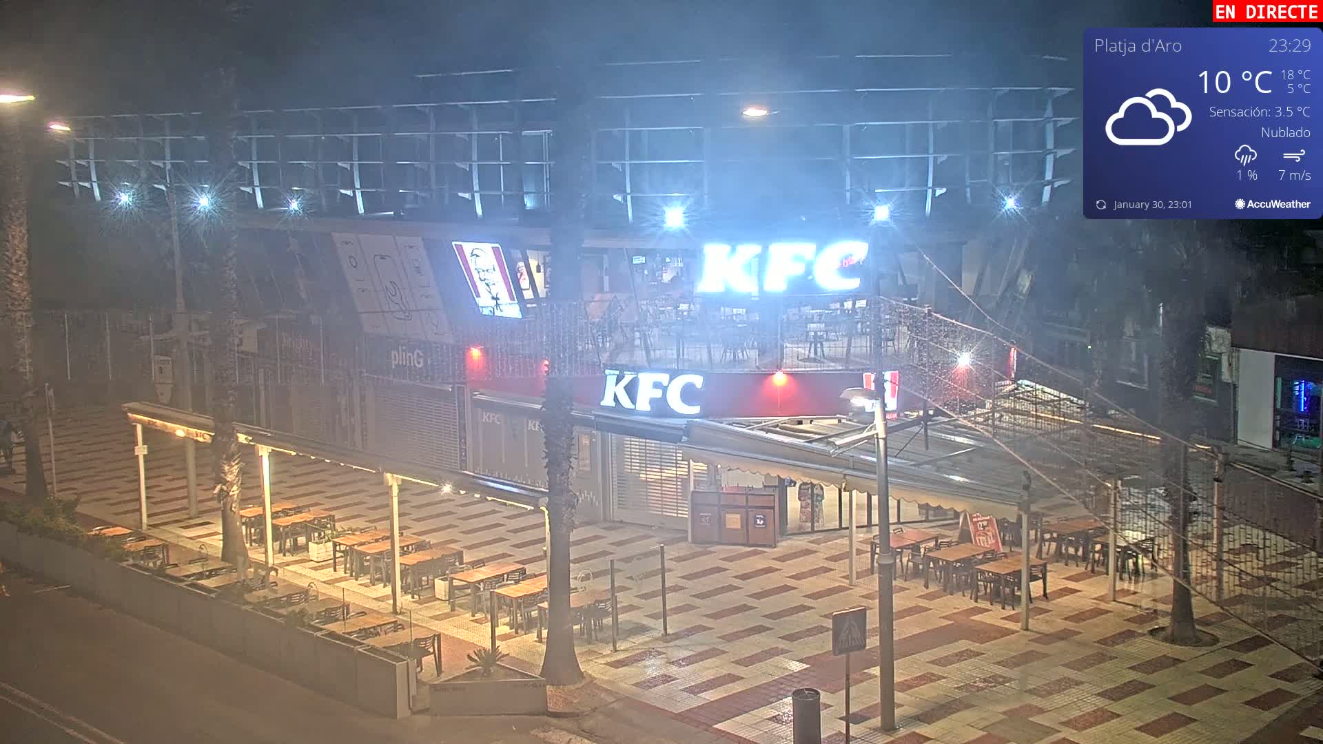 A nighttime, cloudy view of an outdoor KFC restaurant with empty tables and chairs under a covered patio area.