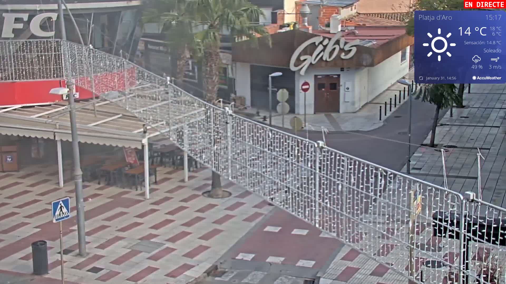 A sunny outdoor scene shows a plaza with a restaurant, string lights, and a pedestrian crossing, under a partly cloudy sky.