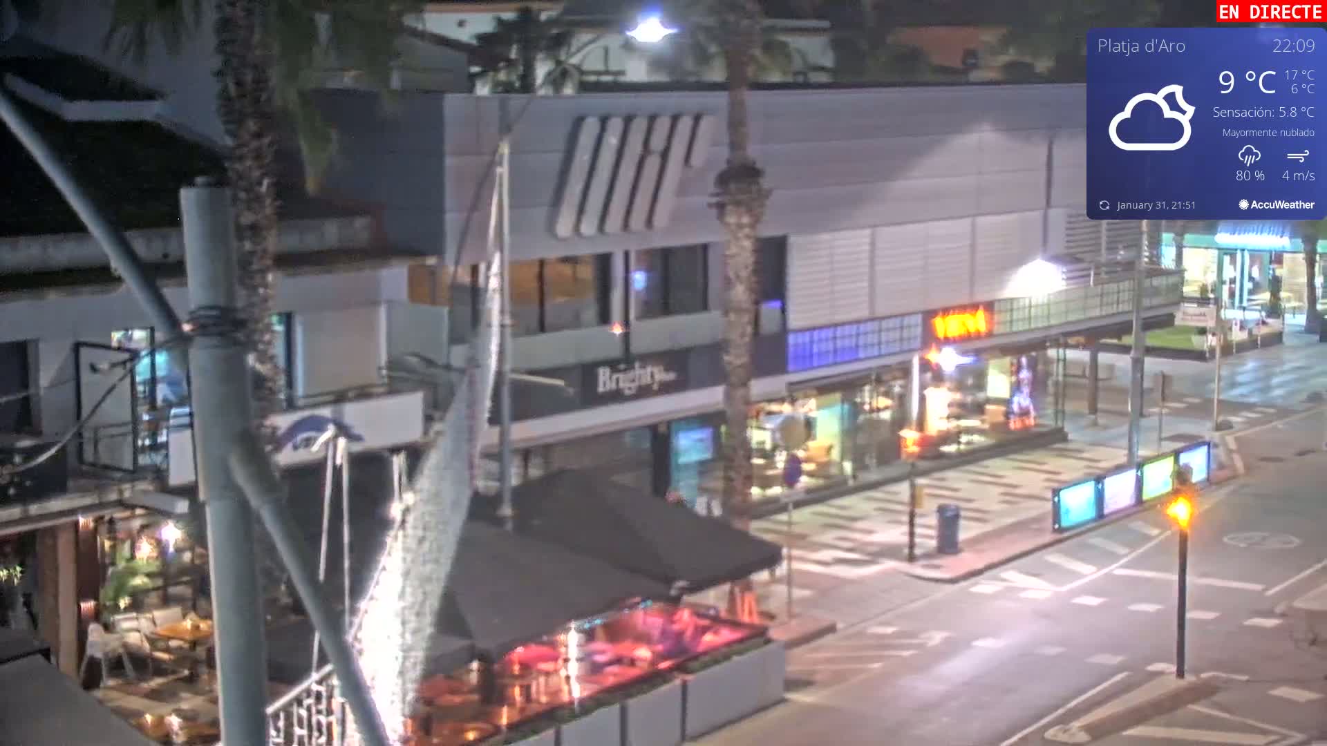 A nighttime street scene shows mostly empty shops and restaurants under mostly cloudy skies.