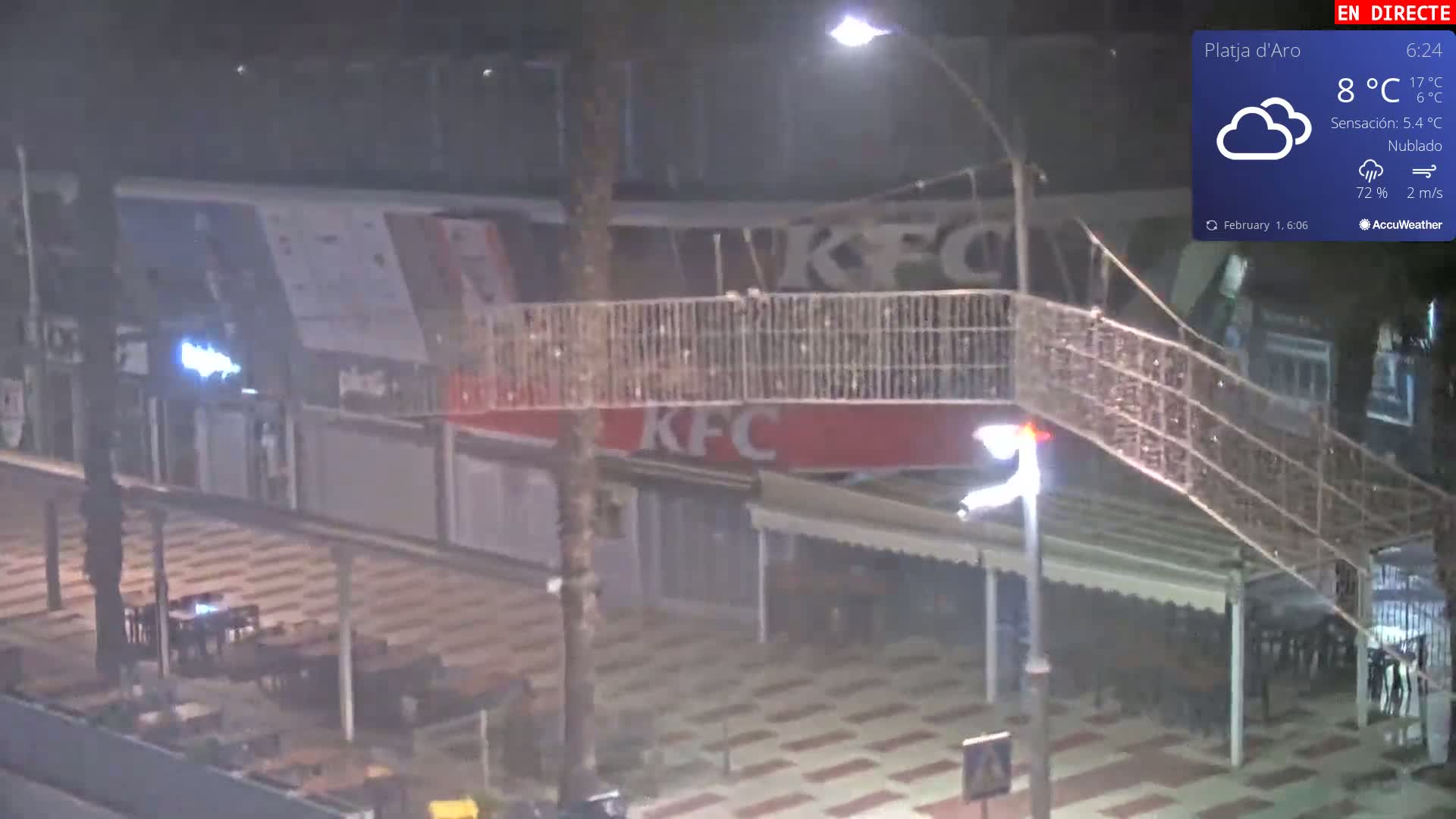 A nighttime, cloudy scene shows a pedestrian bridge above an outdoor seating area in front of a KFC restaurant.