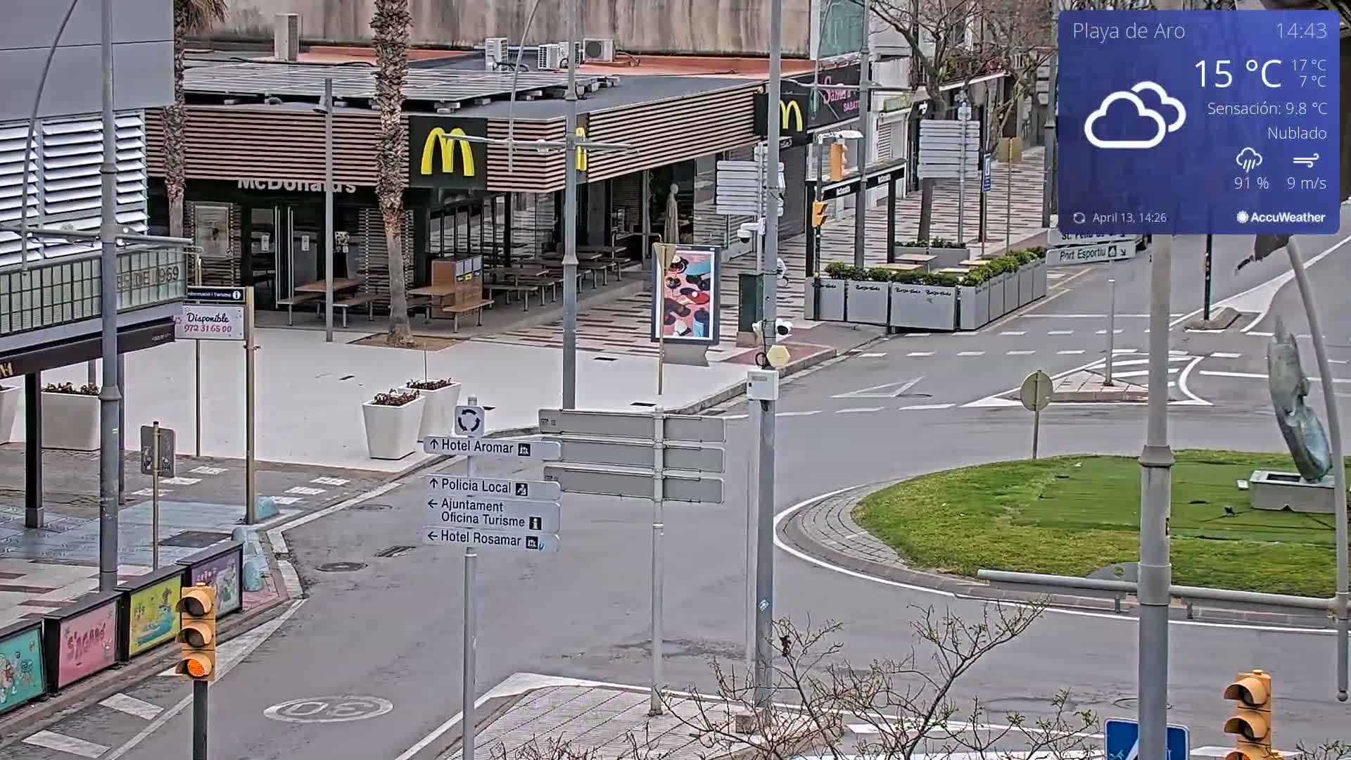 An outdoor plaza with mostly empty tables and chairs in front of a KFC restaurant under partly sunny skies.