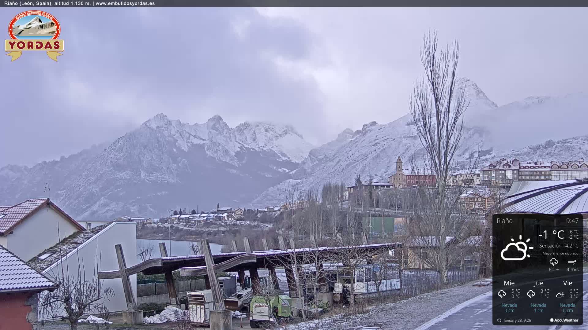 A snow-covered village nestled in a valley between snow-capped mountains under an overcast sky.