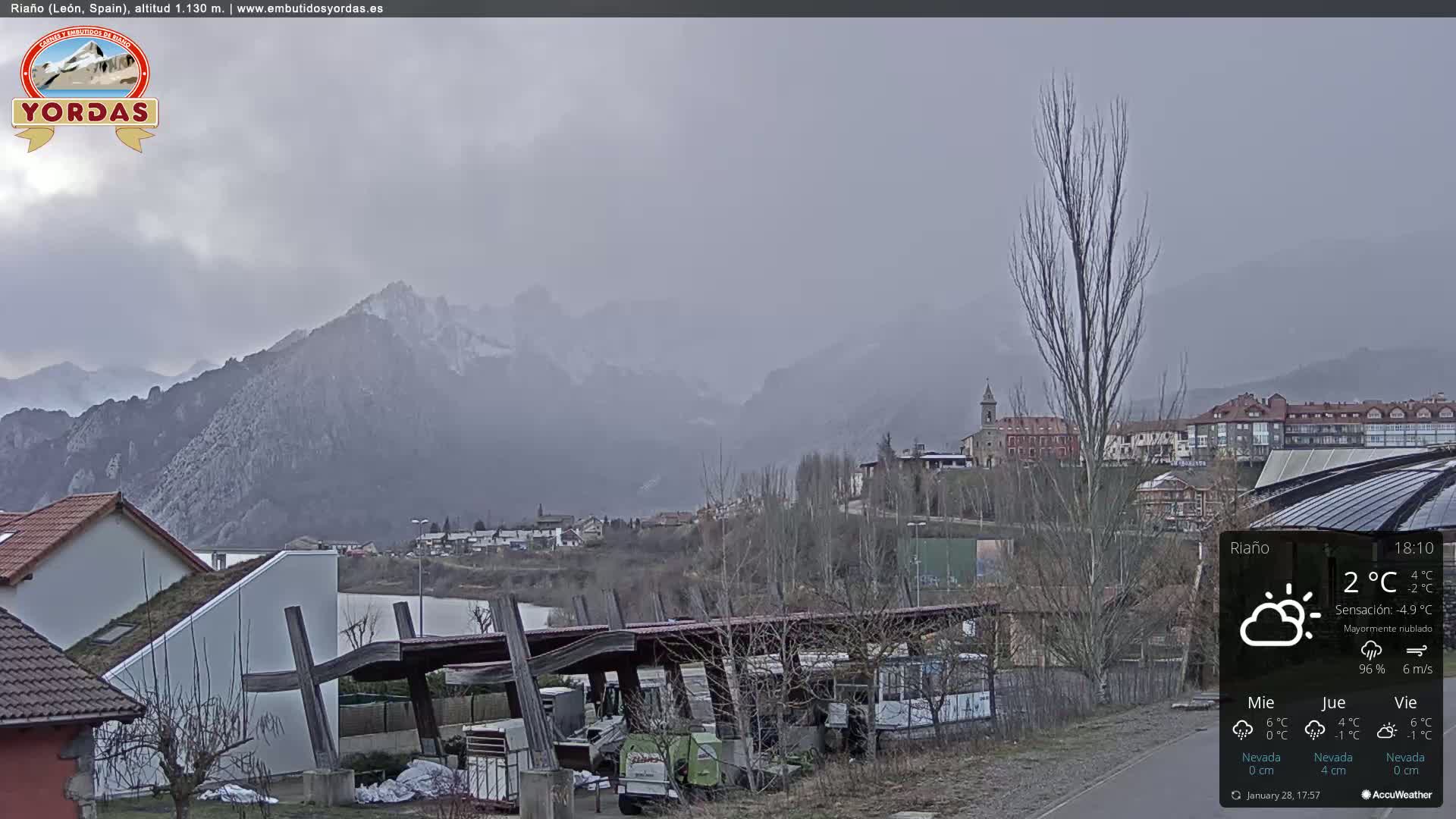 A mostly cloudy view of a town nestled in a valley between snow-dusted mountains.