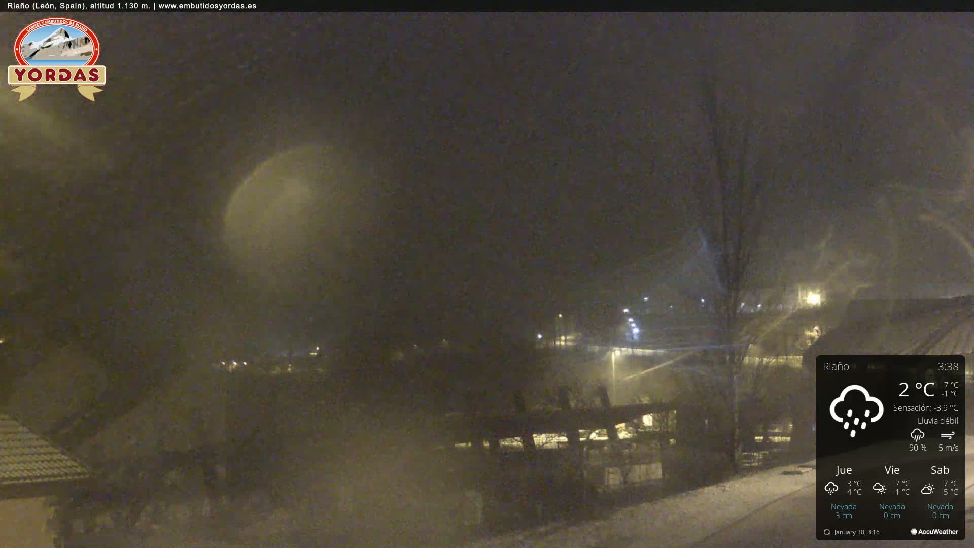 A nighttime scene of a snow-covered town under light snowfall.