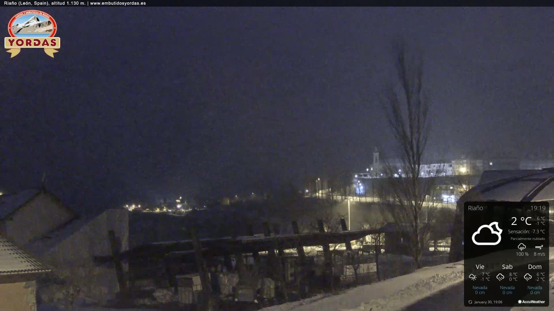 A nighttime, snow-covered town is viewed from a distance under a partly cloudy sky.
