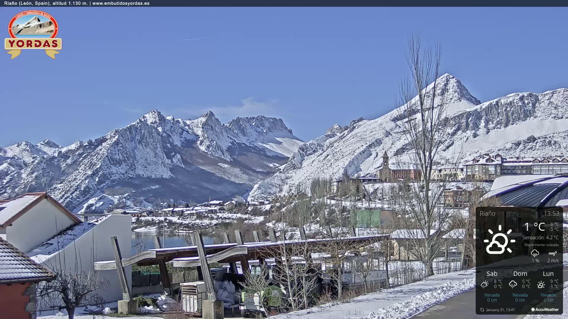 A snow-covered village nestled in a valley between snow-capped mountains under a clear blue sky.