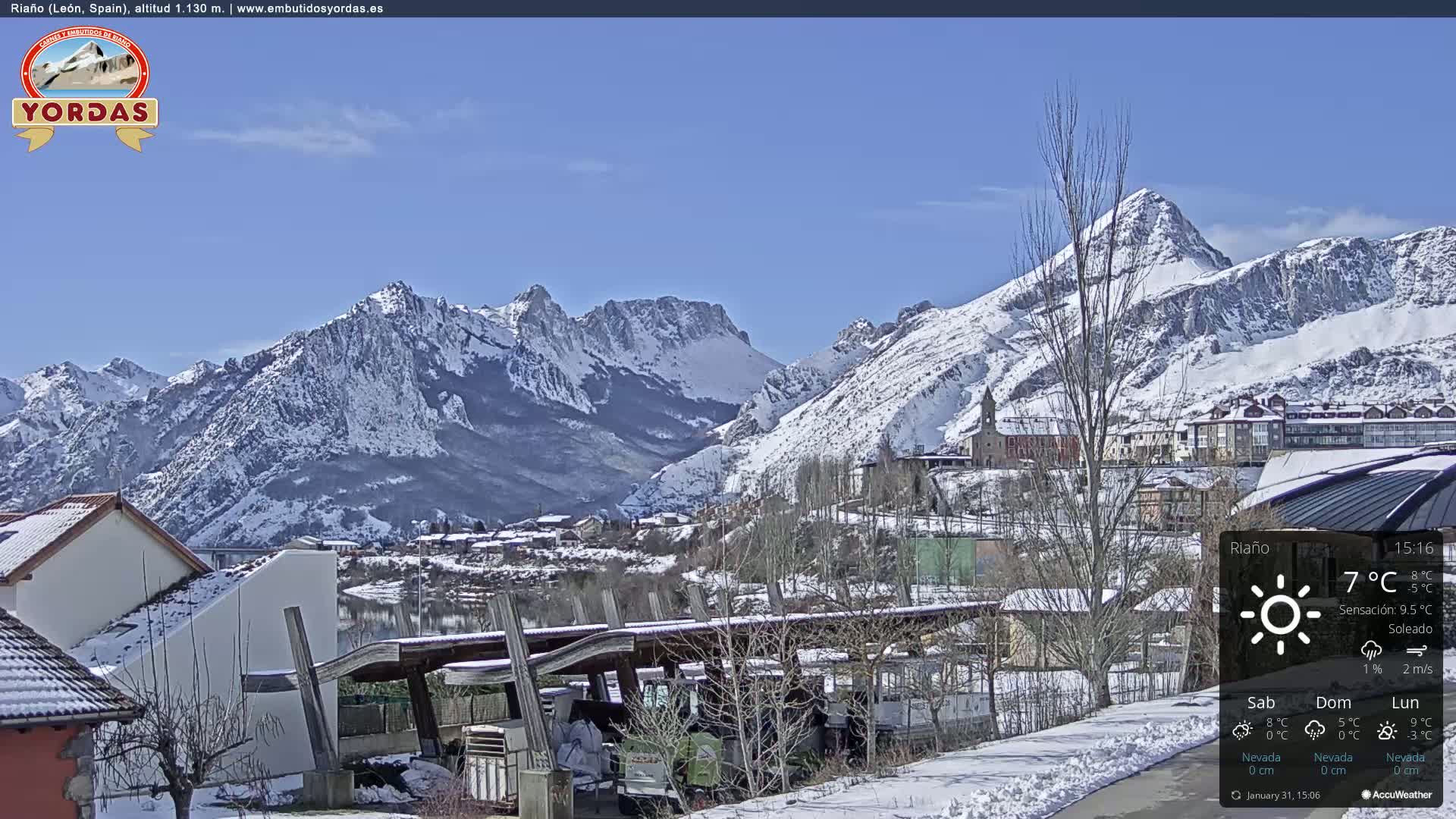 A snow-covered village nestled in a valley between snow-capped mountains under a clear blue sky.