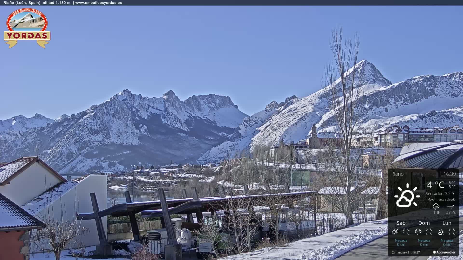 A snow-covered village nestled in a valley between snow-capped mountains under a clear blue sky.