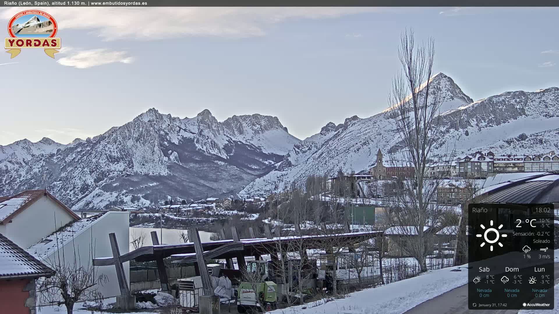 A snowy village nestled in a valley, surrounded by snow-capped mountains under a clear, sunny sky.