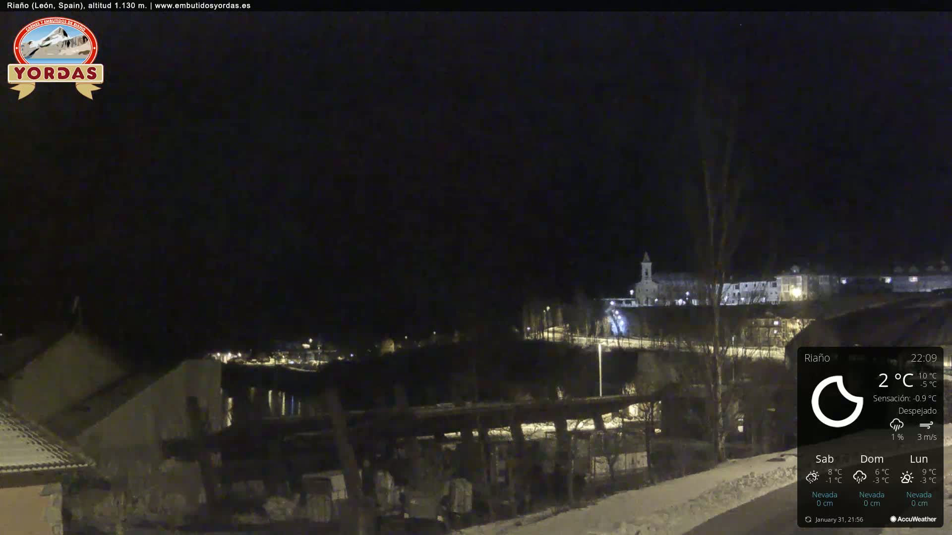 A nighttime view of a snow-covered town with a church steeple in the distance under a clear sky.