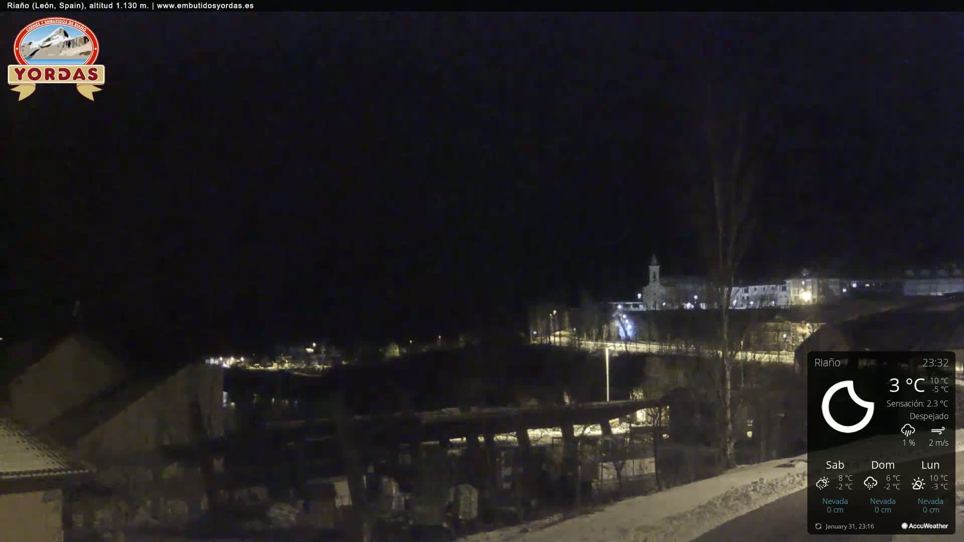 A nighttime view of a snow-covered town, with a clear sky and a few lights visible.