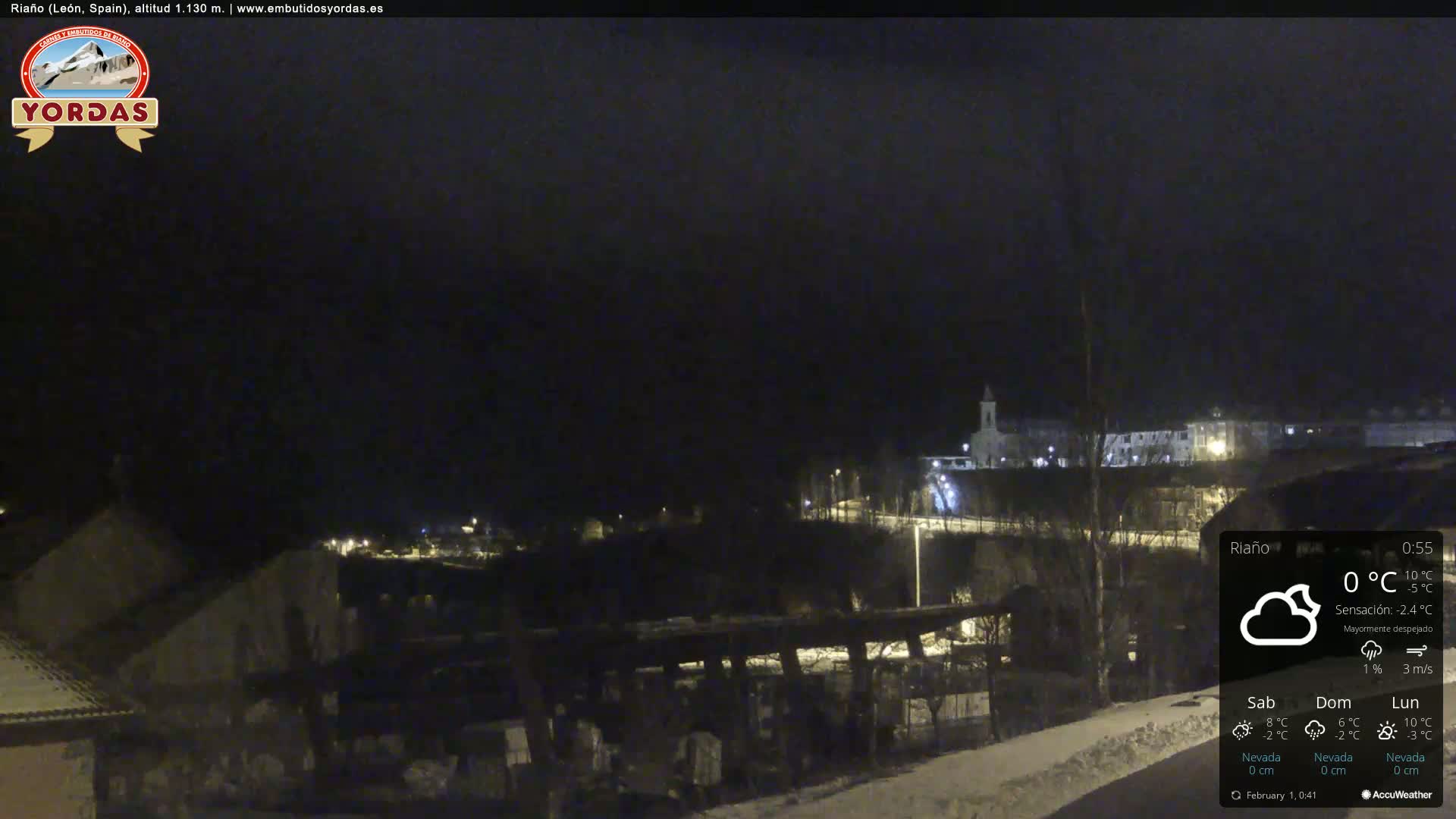 A nighttime view of a small town partially covered in snow, under a mostly clear sky.