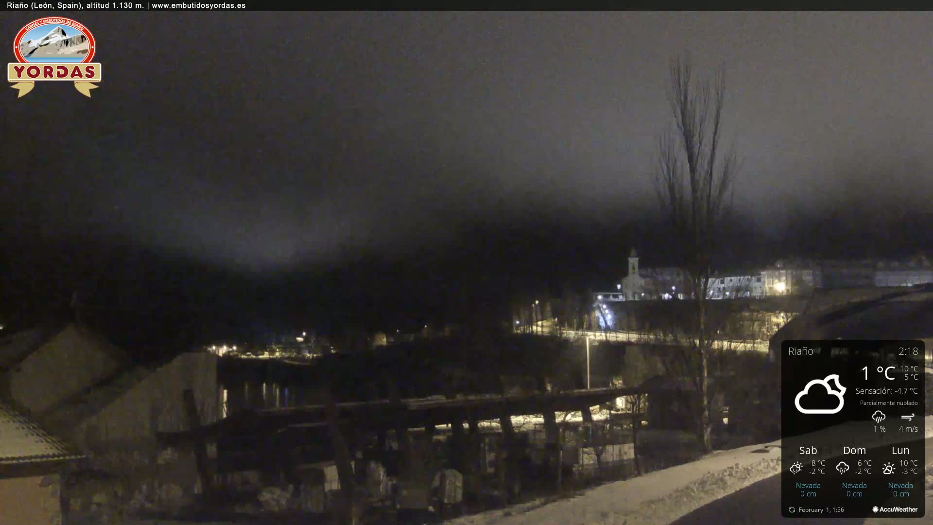A nighttime view of a snow-covered town nestled in a valley under a partly cloudy sky.
