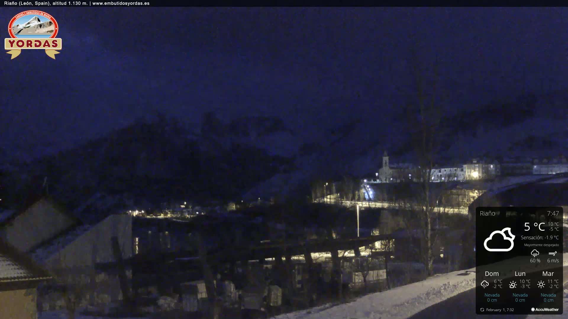 A night-time view of a snow-covered village nestled in a valley between dark mountains under a mostly clear sky.